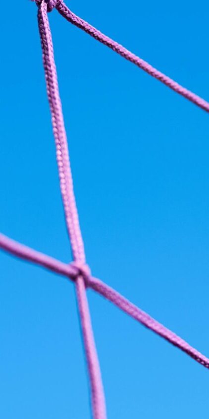 Close-up of a pink volleyball net pattern against a clear blue sky, showcasing geometric shapes.