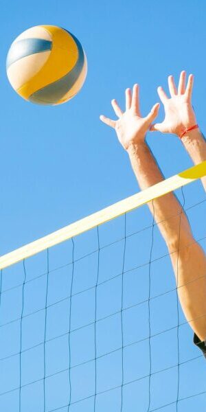 Dynamic outdoor volleyball game with a male player blocking a ball under clear blue skies.